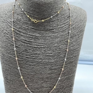 May include: A delicate gold, silver, and rose gold chain necklace with small round beads. The necklace is displayed on a gray mannequin.