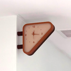 May include: A triangular wall-mounted clock with a light beige face and dark orange frame. The clock features dark orange numerals at the 12, 3, 6, and 9 positions, with simple tick marks for other hours and three thin hands in the center.