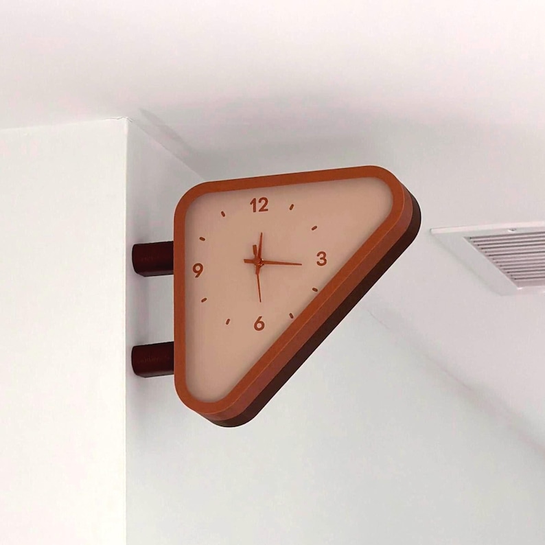 May include: A triangular wall-mounted clock with a light beige face and dark orange frame. The clock features dark orange numerals at the 12, 3, 6, and 9 positions, with simple tick marks for other hours and three thin hands in the center.