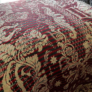 May include: A woven bedspread featuring a complex pattern of cream-colored floral and scroll motifs layered over a background of alternating thin red and black horizontal stripes. The textile has a textured appearance with visible weave details.