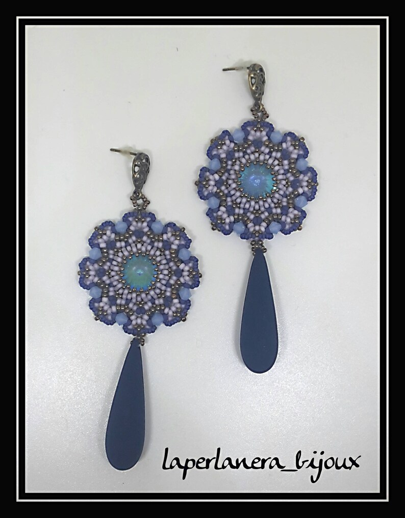 May include: A pair of dangle earrings with a blue, white, and purple beaded flower design and a dark blue teardrop pendant. The earrings are accented with a small iridescent blue stone in the center of each flower.
