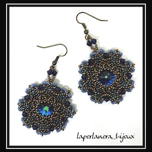 May include: A pair of blue and bronze beaded earrings with a dark blue crystal in the center of each earring. The earrings are hanging from silver hooks. The text "laperlanera_bijoux" is written in black ink at the bottom of the image.
