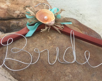 May include: A wooden hanger with a seashell and pearl embellishment and the word "Bride" written in wire.