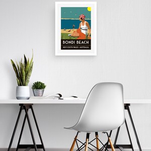 May include: A framed poster with a retro illustration of a woman sitting on a beach in a white swimsuit and red and white polka dot hat. The poster says "Bondi Beach, New South Wales, Australia".