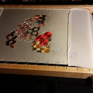 May include: A wooden embroidery hoop with a white fabric stretched across it. The fabric is decorated with colorful embroidered flowers, butterflies, and geometric shapes.