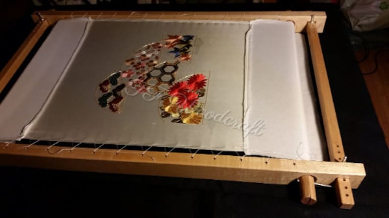 May include: A wooden embroidery hoop with a white fabric stretched across it. The fabric is decorated with colorful embroidered flowers, butterflies, and geometric shapes.