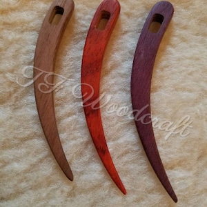 May include: Three wooden crochet hooks, each with a different colour stain. The hooks are curved and have a small hole at the top. The colours are natural wood, red, and purple.