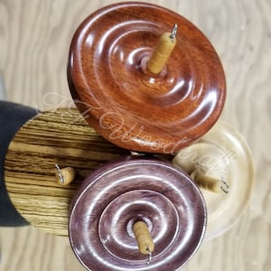 May include: Three wooden spinning wheels with different wood grain patterns. The top wheel is a reddish brown color, the middle wheel is a light brown with dark brown stripes, and the bottom wheel is a dark purple color. Each wheel has a small wooden spindle and a metal hook.
