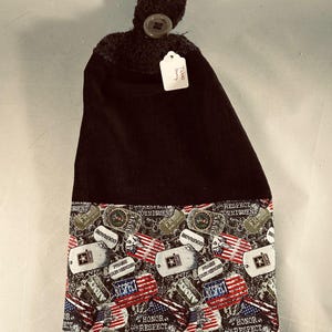 May include: A black hanging kitchen towel with a button closure. The bottom section features a patriotic print with American flags, dog tags, and the words "Honor, Respect, Commitment".