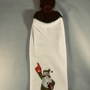 May include: White kitchen towel with a football gnome design. The gnome is wearing a green and white outfit and holding a football. The towel has a dark green crocheted top with a brown button and loop for hanging.