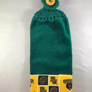 May include: Green kitchen towel with a crocheted top and a yellow button. The bottom of the towel has a yellow and white patterned border with the Baylor University logo and the words "Baylor Bears" and "Baylor University".