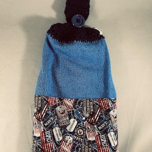 May include: A blue and navy blue kitchen towel with a navy blue crocheted top and button. The bottom of the towel has a patterned design with the word "NAVY", American flags, and military emblems.