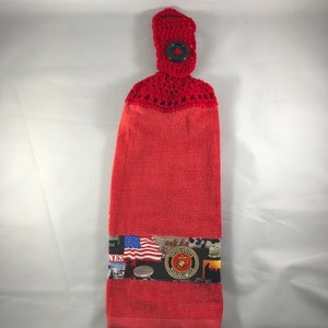 May include: Red crocheted kitchen towel with a loop and button at the top. The towel has a printed band with an American flag, the words "United States Marine Corps", and other military-themed imagery.