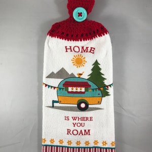 May include: White kitchen towel with a red crocheted hanging loop and a blue button. The towel features a colorful illustration of a camper van, mountains, a pine tree, a bird, and a sun. The text "HOME IS WHERE YOU ROAM" is printed on the towel.