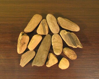 May include: A collection of driftwood pieces in various shapes and sizes, ranging from light to dark brown. The driftwood is arranged in a loose pile on a dark brown wooden surface.