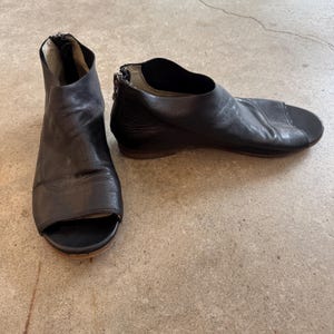 May include: A pair of black leather peep-toe heeled sandals with a zipper on the back.