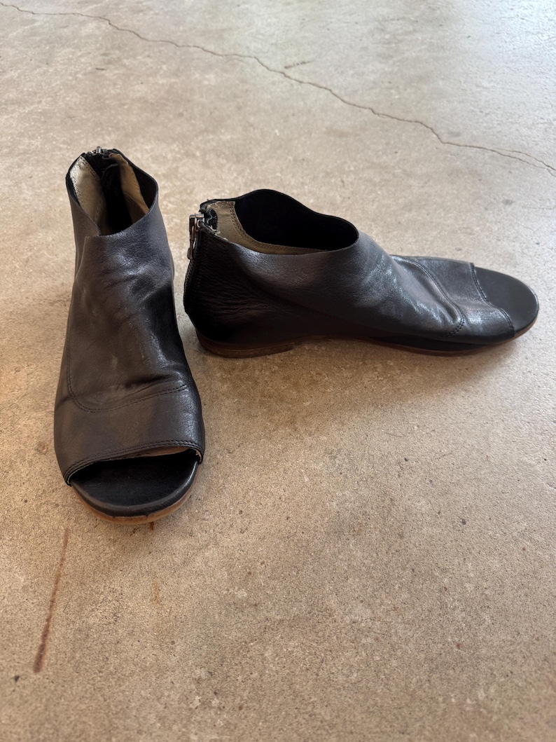 May include: A pair of black leather peep-toe heeled sandals with a zipper on the back.