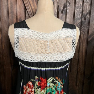 Pu&ograve; includere: Abito nero senza maniche con pannello posteriore in crochet bianco e stampa floreale. L'abito presenta uno scollo quadrato e una gonna a pieghe con un vivace motivo floreale in rosso, verde e blu.