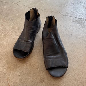 May include: A pair of black leather peep-toe heeled sandals with a zipper on the back.