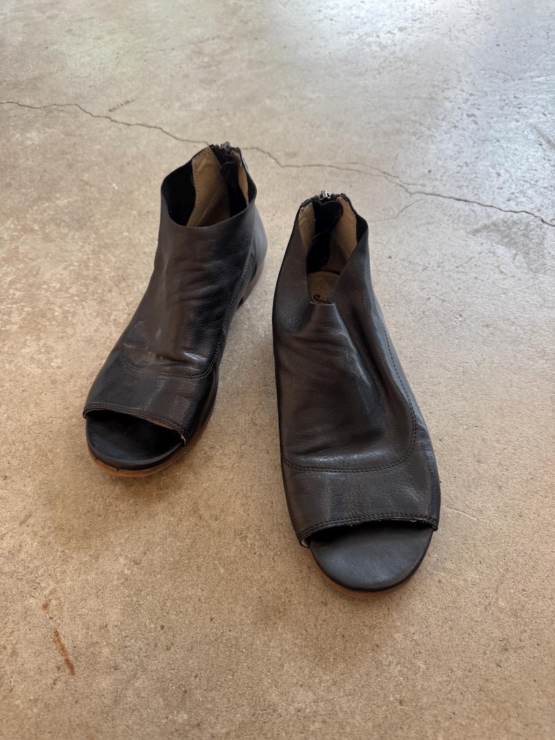 May include: A pair of black leather peep-toe heeled sandals with a zipper on the back.