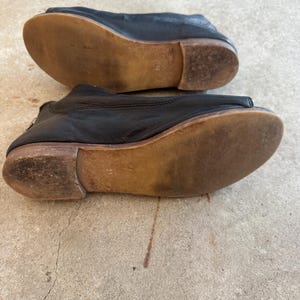 May include: A pair of black leather shoes with a peep toe and a wooden sole. The shoes are worn and have a distressed look.
