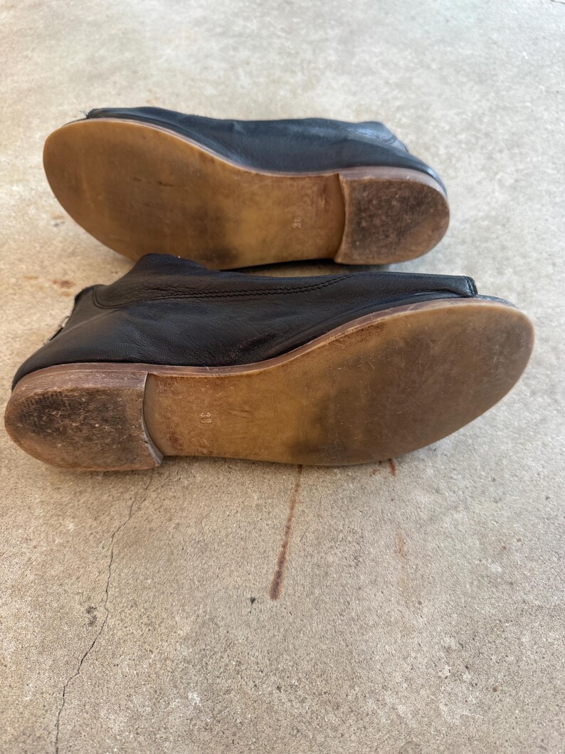 May include: A pair of black leather shoes with a peep toe and a wooden sole. The shoes are worn and have a distressed look.