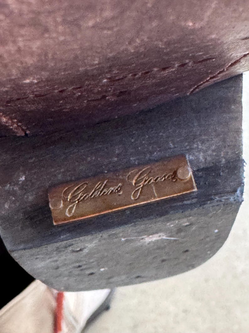 May include: Close-up of a brown leather shoe sole. A small, rectangular, bronze-coloured metal plate is attached to the sole, with the inscription "Golden Goose" in elegant script.