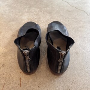 May include: A pair of black leather heeled sandals with a zipper detail on the back. The sandals have an open toe and a cut-out design on the side.