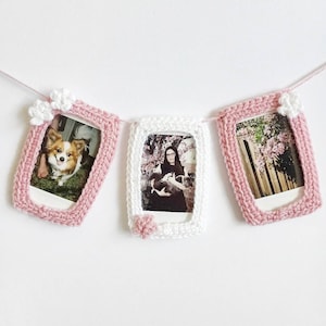 May include: A pink and white crocheted photo garland with three frames. Each frame has a different photo inside. The first frame has a photo of a dog, the second frame has a photo of a woman holding two dogs, and the third frame has a photo of a flowering tree.