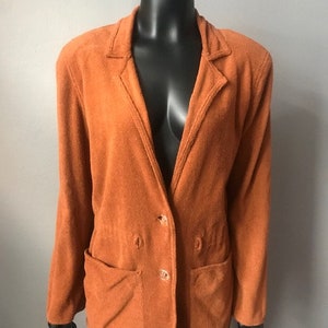 Può includere: Un blazer color arancio bruciato con maniche lunghe, due tasche e chiusura con bottoni.