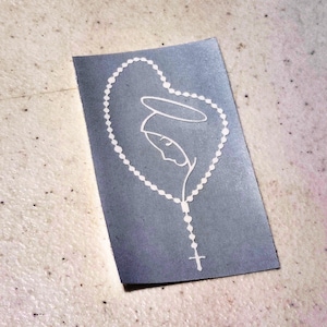 May include: A white vinyl decal of a woman with a halo and a rosary. The decal is on a gray background.