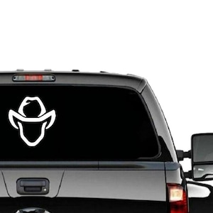 May include: A white silhouette of a cowboy hat and face on a black truck tailgate.