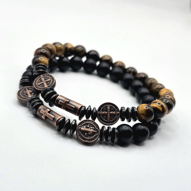 Peut inclure: Deux bracelets de perles superpos&eacute;s. L'un est compos&eacute; de perles &oelig;il de tigre et noires. L'autre pr&eacute;sente des perles noires, des croix et des m&eacute;daillons en bronze.