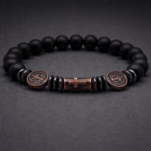 Peut inclure: Bracelet de perles noires avec des accents de croix et de m&eacute;daillon de couleur bronze. Le bracelet pr&eacute;sente des perles noires mates, des entretoises m&eacute;talliques et une perle centrale en forme de croix. Les m&eacute;daillons ont un design d&eacute;taill&eacute;.