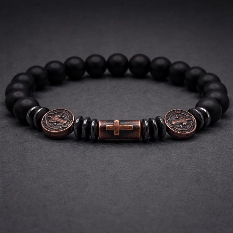 Peut inclure: Bracelet de perles noires avec des accents de croix et de m&eacute;daillon de couleur bronze. Le bracelet pr&eacute;sente des perles noires mates, des entretoises m&eacute;talliques et une perle centrale en forme de croix. Les m&eacute;daillons ont un design d&eacute;taill&eacute;.