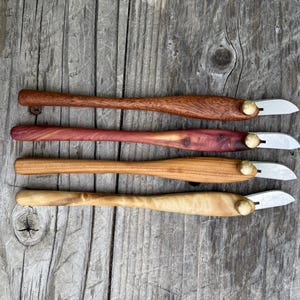 Puede incluir: Cuatro cuchillos de tallado de madera hechos a mano con diferentes mangos de madera y pequeñas hojas curvas. Los mangos varían en color de marrón claro a oscuro, con un remache de color latón que asegura la hoja.