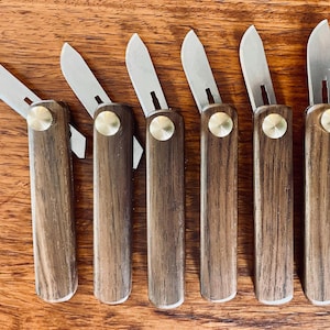 May include: Seven small, wooden handled pocket knives with silver blades. The handles are made of dark wood with a brass accent.