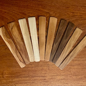 May include: A set of ten wooden spatulas in various shades of brown, arranged in a fan shape on a wooden surface.