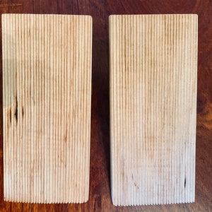 Op de afbeelding: Twee houten blokken met een gegroefde textuur. De blokken zijn lichtbruin van kleur en hebben een natuurlijke houten afwerking.