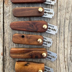 May include: A white ceramic mug with a black handle and the text "But First, Coffee" in a bold, black font. The mug is set against a blurred background, suggesting a cosy setting.