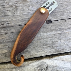 May include: A handcrafted, wooden straight razor with a curved handle and a stainless steel blade. The razor features a dark brown wood grain and a brass-colored rivet. The blade is marked with the word "ORCO" and "STAINLESS BLADE".