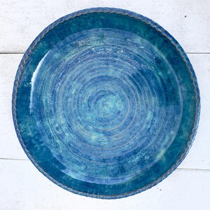 May include: A handmade ceramic plate with a vibrant blue glaze. The plate features concentric circular grooves and a scalloped edge. The color transitions from a deep teal to a lighter turquoise, creating a textured appearance. This decorative plate is ideal for serving food.