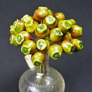 May include: A decorative glass vase with a bouquet of green and red ceramic apples. The apples have a glossy finish and are arranged on thin metal stems. The vase is clear with etched patterns.