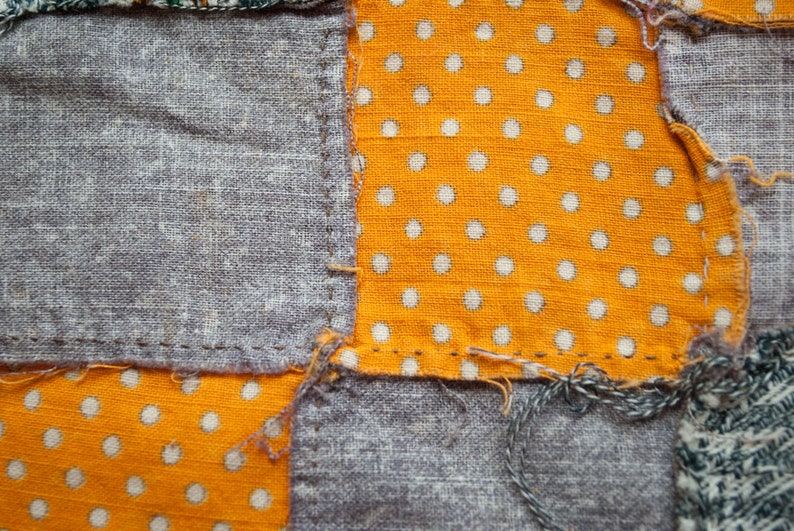 Pu&ograve; includere: Primo piano di un tessuto patchwork con quadrati di tessuto grigio e tessuto arancione a pois bianchi. I pezzi sono cuciti insieme con filo visibile, mostrando un'estetica fatta a mano.