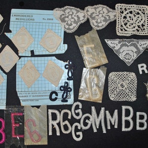 Puede incluir: Una colección de artículos bordados vintage, que incluyen medallones en forma de diamante con letras, tapetes de encaje y letras bordadas individuales en varias fuentes y colores. Algunos artículos aún están en su embalaje original.