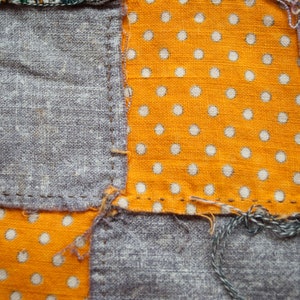 Pu&ograve; includere: Primo piano di un tessuto patchwork con quadrati di tessuto grigio e arancione. Il tessuto arancione ha pois bianchi. I pezzi sono cuciti insieme con filo visibile, mostrando un aspetto fatto a mano.