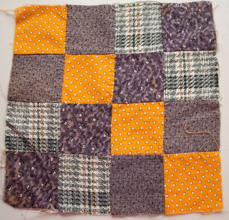 Pu&ograve; includere: Un quadrato patchwork composto da sedici quadrati di tessuto in vari modelli e colori. I colori includono giallo senape con pois bianchi, grigio con piccoli motivi floreali e quadri verdi e bianchi.