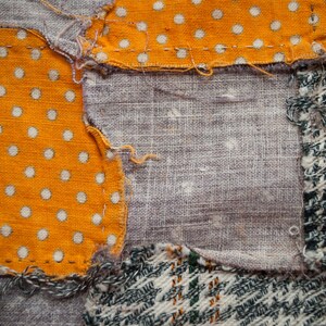 Pu&ograve; includere: Primo piano di un tessuto patchwork con vari modelli di tessuto. Il design include una sezione di tessuto arancione con pois bianchi, lino grigio e un motivo simile al tweed verde e bianco. I pezzi sono cuciti insieme con filo visibile.