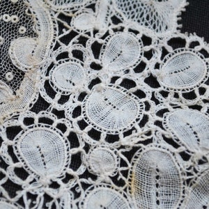 May include: Close-up of antique white lace with intricate floral and circular patterns. The delicate textile features detailed openwork and a scalloped edge, showcasing the craftsmanship of vintage lace.