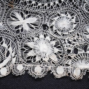 May include: Close-up of a section of white lace with intricate floral and geometric patterns. The lace features circular and fan-shaped designs, creating a delicate and textured appearance. The detailed craftsmanship is evident in the fine, interconnected threads. This textile is suitable for various craft projects.